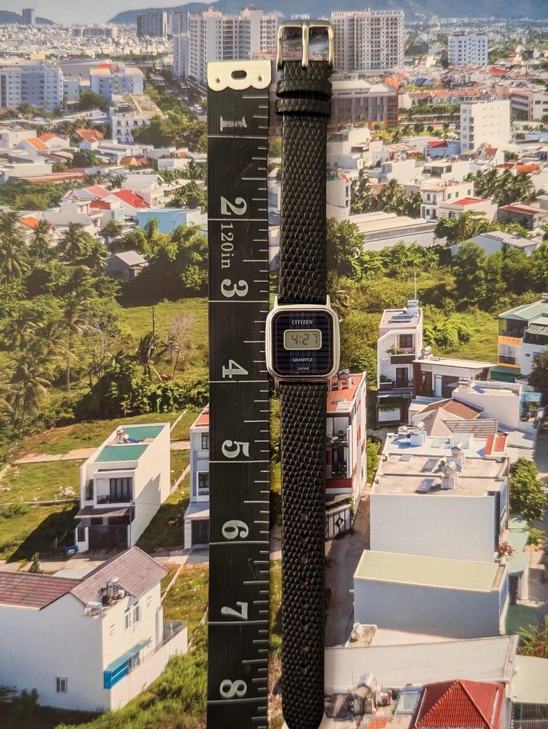 May include: A vintage Citizen Quartz watch with a black textured band and silver buckle. The watch face displays the time as 4:27. The watch is approximately 8 inches long, measured with a black ruler.