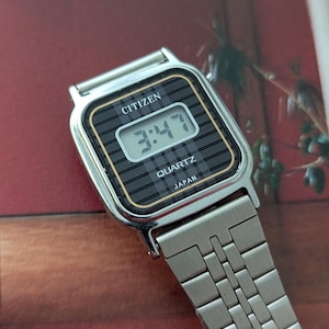 May include: A silver Citizen Quartz watch displaying the time 3:47. The watch has a black face with a grid pattern and gold trim. The watchband is made of silver metal links.