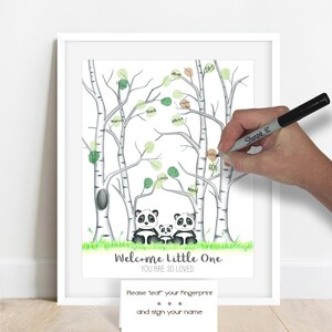 May include: A framed print featuring a family of pandas beneath birch trees with green leaves. The words "Welcome Little One, You Are So Loved" are at the bottom. A person is using a black marker to add a fingerprint and name to the tree.