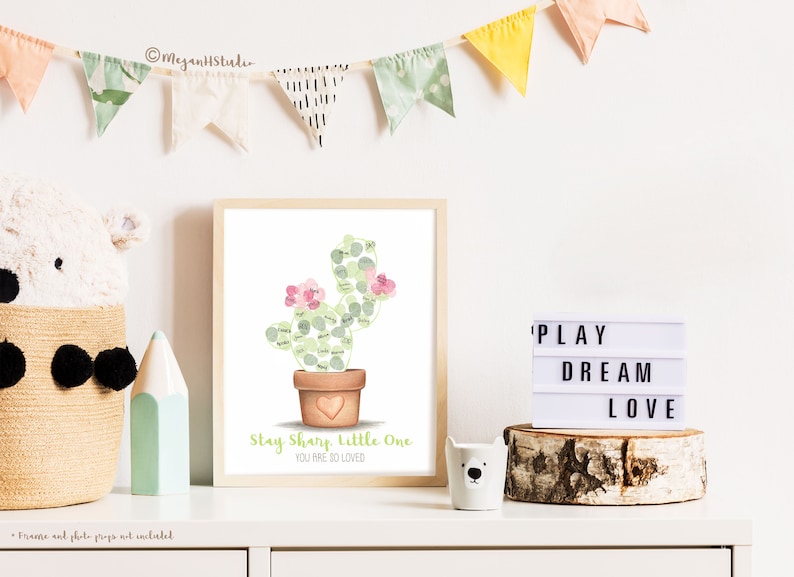 completed cactus themed fingerprint guestbook in a frame and displayed in a neutral themed nursery shown with fingerprints from friends and family added to fill in the outline of a cactus on an art print of my hand drawn original, meganhstudio