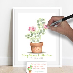 example of a guest adding their signature to their fingerprint on a fingerprint cactus guestbook alternative, fingerprints are made with stamp pad ink and used to fill in the outline of a hand drawn cactus shown in a terra cotta pot meganhstudio