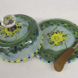 May include: A ceramic butter dish with a matching plate and butter knife. The dish and plate are painted with a light blue background, green and yellow accents, and a decorative crystal knob on the lid.