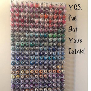 May include: A white pegboard wall display holding numerous spools of sewing thread arranged in a color gradient from pinks and reds at the top to blues, greens, and purples at the bottom. The text Yes, I've got Your Color! is printed on the right.