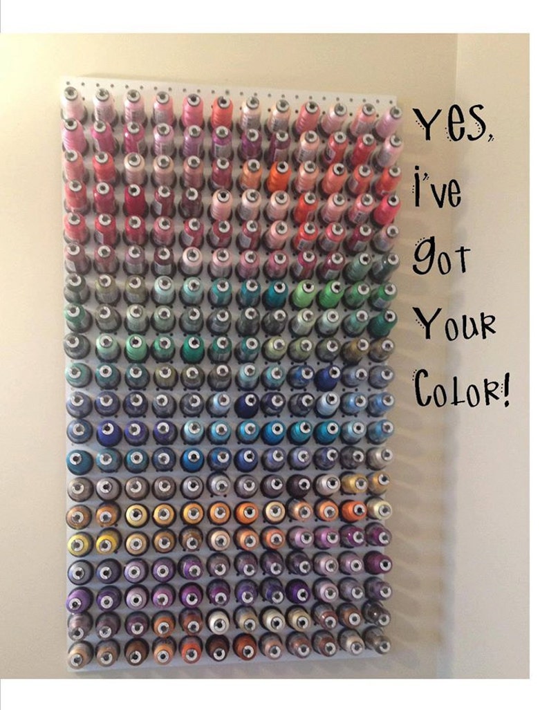 May include: A white pegboard wall display holding numerous spools of sewing thread arranged in a color gradient from pinks and reds at the top to blues, greens, and purples at the bottom. The text Yes, I've got Your Color! is printed on the right.