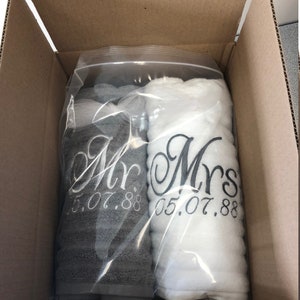 May include: Two rolled towels, one dark gray and one white, packaged in a clear plastic bag. The gray towel is embroidered with the text "Mr." and "05.07.88" in white, while the white towel features the text "Mrs." and "05.07.88" in dark gray.