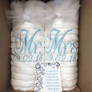 May include: Two white towels rolled and tied with white tulle bows, embroidered with light blue script reading Mr. and Mrs. above the date 09.02.18. A white card with black swirling patterns and text reads: Congratulations! Sad we couldn't make it but we are there in spirit! May you always know how to love, listen to & heal each other. Love, The Taylors.