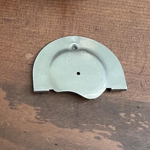 May include: A silver-colored, semi-circular metal object with a circular indentation and two holes. The object has a flat edge and is set against a wooden surface.