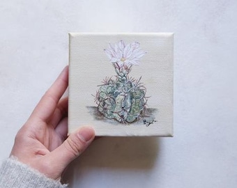 May include: A small painting on canvas of a cactus with a single pink flower. The cactus is green and has a spiky texture. The painting is on a white background.