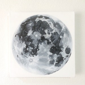 Pode incluir: Uma pintura em preto e branco de uma lua cheia em uma tela branca. A lua &eacute; pintada em detalhes, mostrando suas crateras e caracter&iacute;sticas da superf&iacute;cie. A assinatura do artista &eacute; vis&iacute;vel no canto inferior direito.