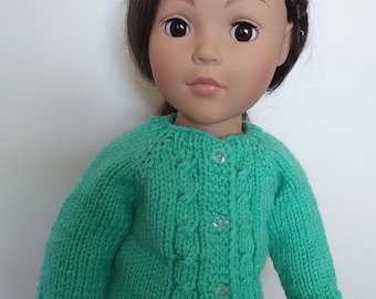May include: A doll with brown hair styled in a braided headband, wearing a bright green long-sleeved knit cardigan. The cardigan features a vertical cable knit pattern down the front, a round neckline, and four clear buttons for closure.