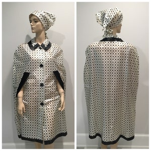 May include: A white raincoat with black polka dots and a black trim. The raincoat has a collar and a button closure. It is paired with a matching black and white polka dot headscarf.