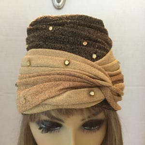 May include: A vintage turban-style hat in shades of brown and gold, adorned with small, round, gold-colored embellishments. The hat features a layered design with a knotted detail, creating a stylish and elegant look.