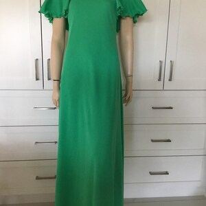 May include: A long, green maxi dress with short sleeves and a ruffled trim. The dress has a round neckline and is made of a smooth, flowing fabric.
