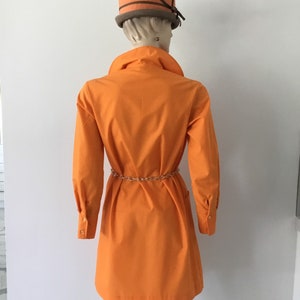 Op de afbeelding: Een feloranje getailleerde jurk met lange mouwen en een riem. De jurk heeft een eenvoudig, klassiek ontwerp en is gemaakt van een lichtgewicht stof.