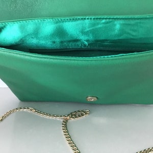 May include: A green leather clutch purse with a gold chain strap. The purse has a flap closure and a small pocket on the inside.