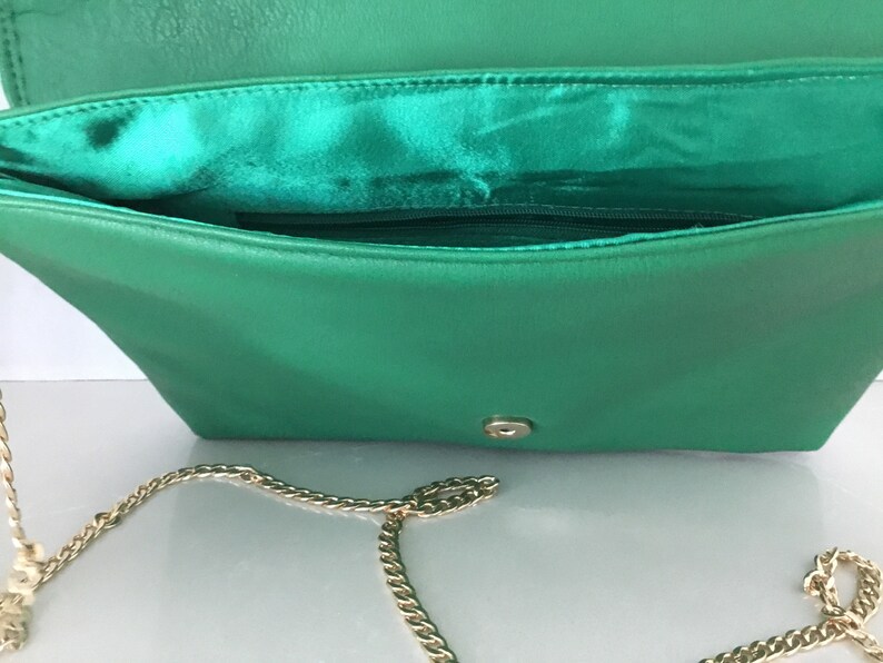 May include: A green leather clutch purse with a gold chain strap. The purse has a flap closure and a small pocket on the inside.