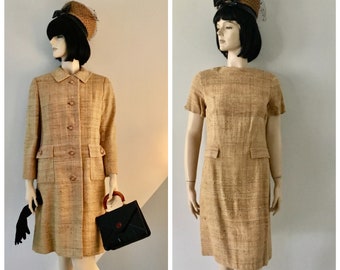 May include: A tan tweed dress with short sleeves and a matching coat. The dress has a simple, fitted silhouette and a round neckline. The coat has a button-up front and two pockets. Both pieces are made of a textured fabric.