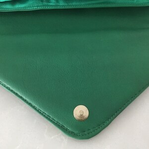 May include: A green leather clutch purse with a gold-toned button closure.