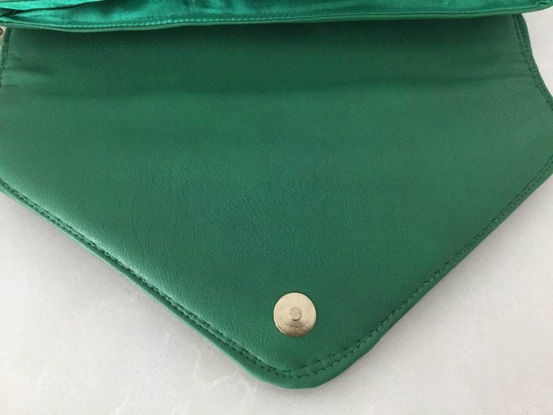 May include: A green leather clutch purse with a gold-toned button closure.
