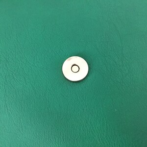 May include: A close-up of a green leather surface with a silver snap closure.