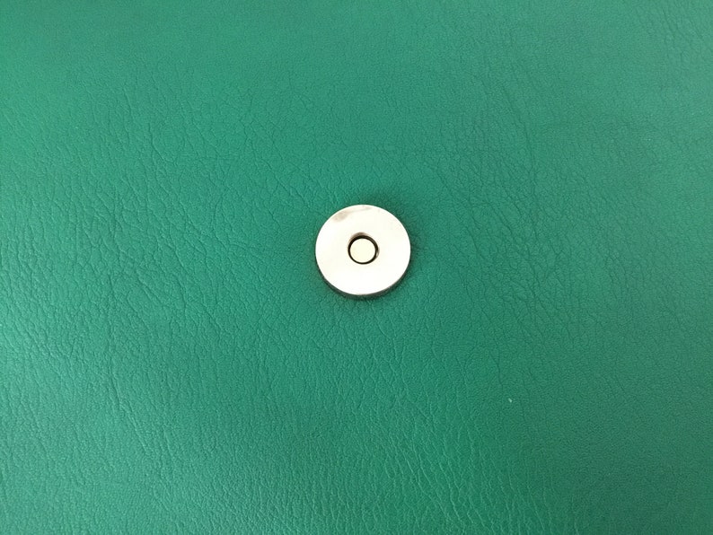 May include: A close-up of a green leather surface with a silver snap closure.