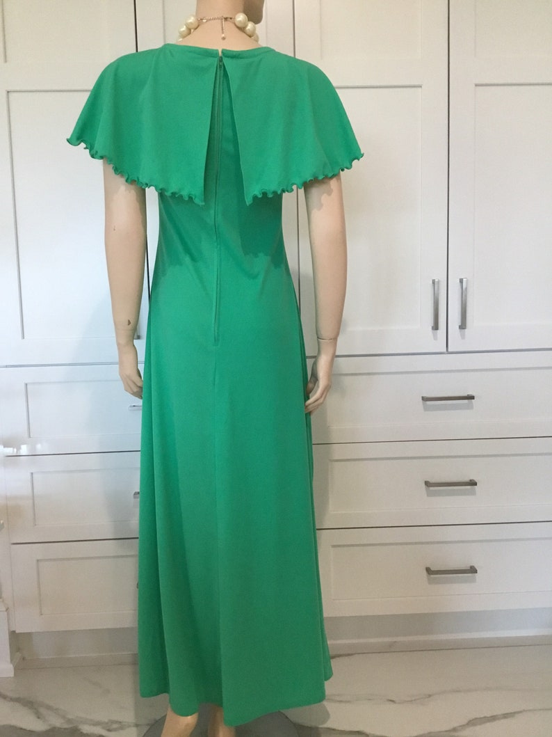 May include: A long green maxi dress with a cape-like collar and short sleeves. The dress has a zipper down the back.