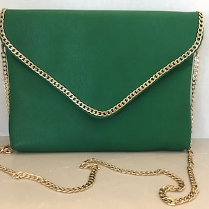 May include: A green leather envelope clutch with a gold chain strap. The clutch has a flap closure and a gold chain trim around the edges.