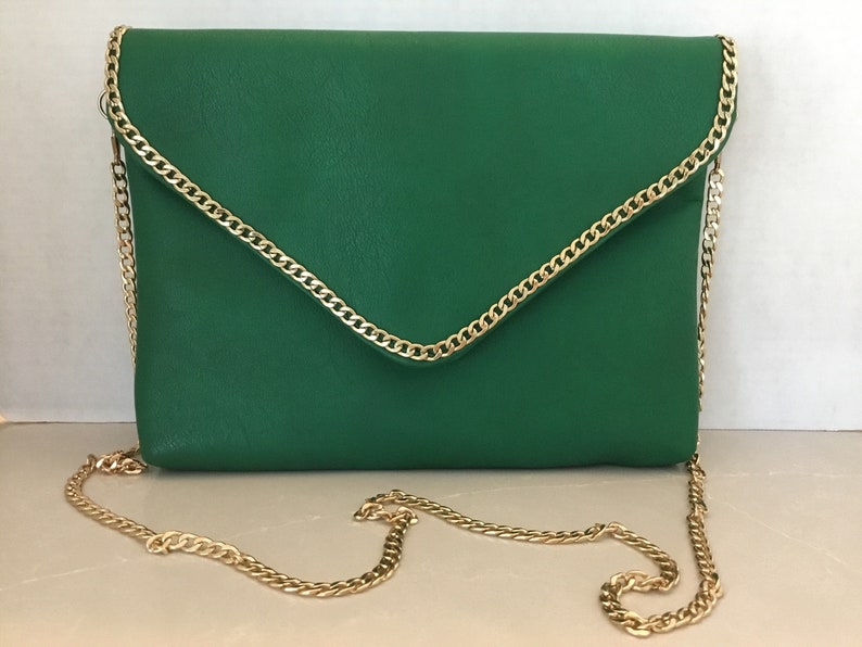 May include: A green leather envelope clutch with a gold chain strap. The clutch has a flap closure and a gold chain trim around the edges.