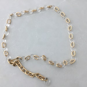 Op de afbeelding: Een transparante plastic ketting met gouden accenten. De ketting is in een cirkel aan elkaar gekoppeld en heeft een gouden sluiting.