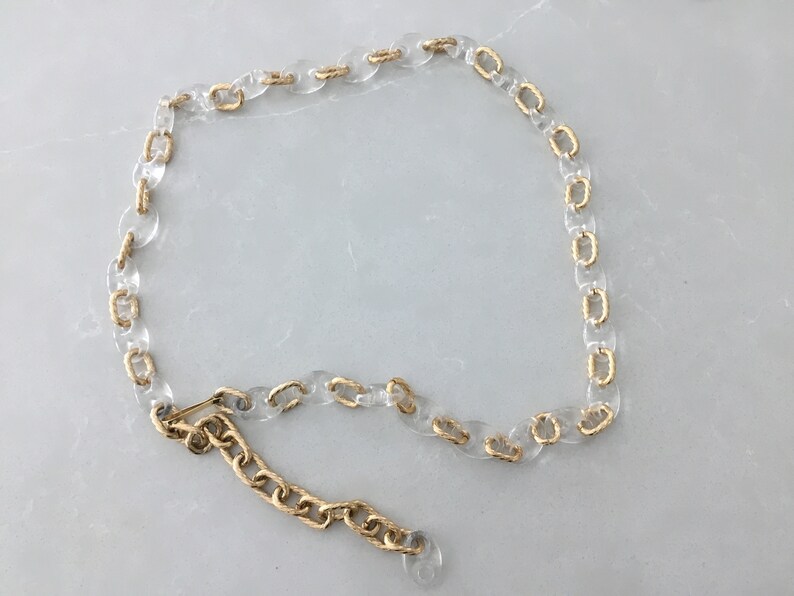 Op de afbeelding: Een transparante plastic ketting met gouden accenten. De ketting is in een cirkel aan elkaar gekoppeld en heeft een gouden sluiting.