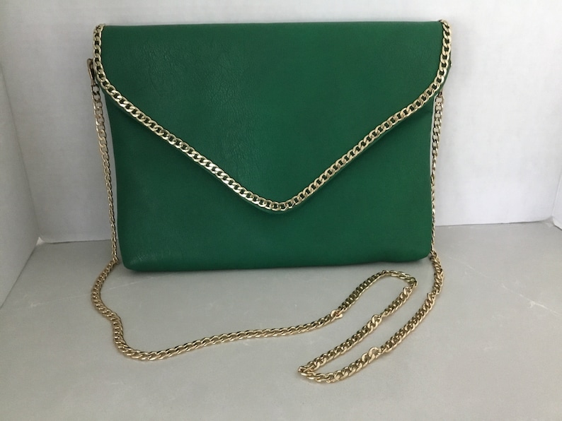 May include: A green leather clutch with a gold chain strap. The clutch has a flap closure and a gold chain trim.