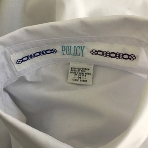 K&ouml;nnte beinhalten: Wei&szlig;es Hemd mit Kragen und einem Etikett mit der Aufschrift "POLICY" und dem Text "65% POLYESTER 35% COTTON MADE IN HONG KONG RM 57773 ---M--- (CARE OVER)"