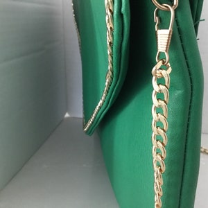 May include: A green leather clutch bag with a gold chain strap. The bag has a flap closure and a gold chain trim.