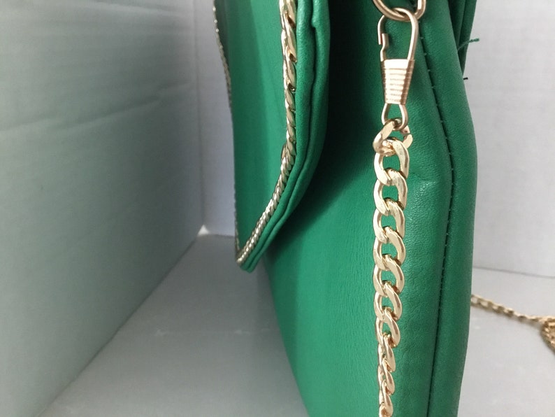 May include: A green leather clutch bag with a gold chain strap. The bag has a flap closure and a gold chain trim.