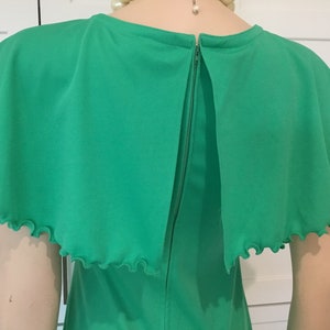 May include: A green dress with a cape-like top and a ruffled trim. The dress has a back zipper closure.