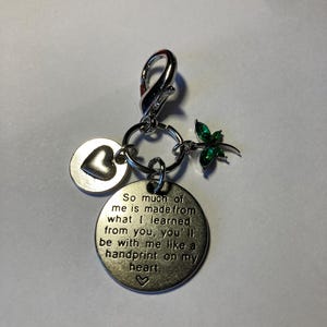 May include: Silver charm with a heart, a four-leaf clover with green rhinestones, and a round tag with the text "So much of me is made from what I learned from you, you'll be with me like a handprint on my heart."
