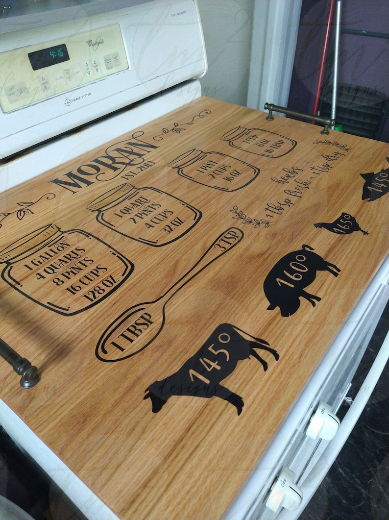 May include: A wooden stovetop cover with a black design featuring a spoon, jars with measurements, and animals. The text "MORAN EST. 2013" is printed on the cover.