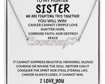 May include: A silver necklace with a heart charm and the name "Courtney" engraved on it. The necklace comes in a white box with a message of support for a sister fighting cancer. The message reads: "To my fighter sister, we are fighting this together, you will win! Cancer cannot cripple love, shatter hope, corrode faith, nor destroy peace. It cannot suppress beautiful memories, silence courage or invade the soul. Neither can it conquer the spirit nor steal eternal life. Cancer always loses, it cannot win. I love you."