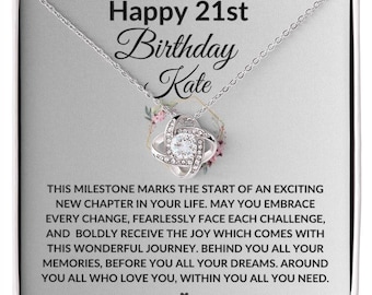 May include: A silver necklace with a knot pendant and a clear crystal in the center. The necklace is in a white box with a message that reads "Happy 21st Birthday Kate. This milestone marks the start of an exciting new chapter in your life. May you embrace every change, fearlessly face each challenge, and boldly receive the joy which comes with this wonderful journey. Behind you all your memories, before you all your dreams. Around you all who love you, within you all you need."