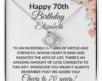 May include: A silver necklace with a crystal knot pendant in a white gift box with a floral design. The box has a message that reads "Happy 70th Birthday Elizabeth. To an incredible woman of virtue and strength, whose heart is kind and radiates the joys of life. There's an amazing amount of love connected to this gift. Whenever you wear it always remember that we adore you! Cheers to 70 years!"