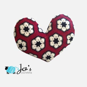 Puede incluir: Un cojín de corazón de punto de ganchillo rojo, blanco y negro con un patrón floral.