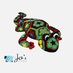 May include: A colorful, crocheted lizard toy in a patchwork design. The lizard features a variety of colors including red, green, yellow, and blue. The toy is handmade and has a whimsical appearance. The logo "Jo's crocheteria" is in the bottom left corner.