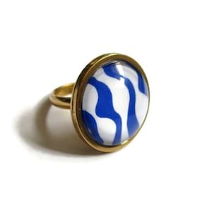 Könnte beinhalten: Ein goldener Ring mit einem blauen und weißen abstrakten Muster auf der Oberseite. Der Ring ist rund und hat eine glatte Oberfläche.