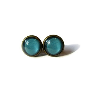 May include: A pair of teal blue glass stud earrings with bronze settings.