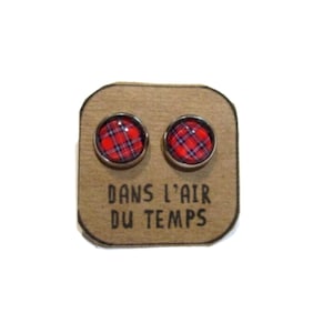 Op de afbeelding: Een paar zilveren oorbel studs met rood en blauw ruitpatroon. De oorbellen worden getoond op een bruine kaart met de tekst "Dans l'air du temps".