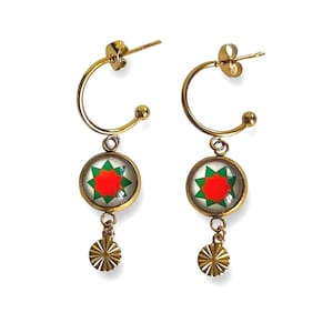 Puede incluir: Pendientes de aro dorados con un colgante con un diseño de estrella roja y verde. El colgante está unido a un pequeño disco dorado.