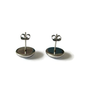 May include: A pair of silver stud earrings with a round, dark blue cabochon stone in the center.