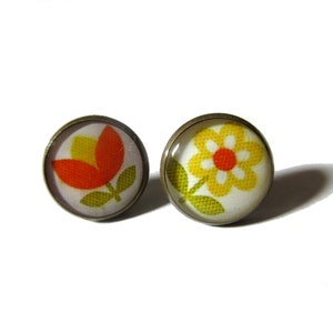 May include: A pair of earrings with a flower design. One earring features a red and yellow tulip, while the other features a yellow daisy with a red center. Both earrings have a white background and are set in a bronze-colored metal.