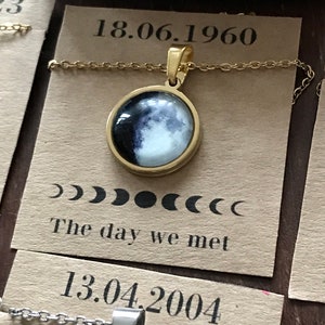Può includere: Due collane d'oro con ciondoli a forma di luna. La prima collana ha un ciondolo a forma di luna con la data 18.06.1960 e il testo "The day we met". La seconda collana ha la data 13.04.2004.