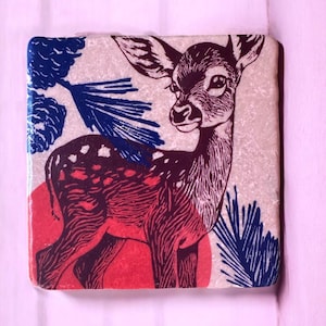 Könnte beinhalten: Quadratischer Untersetzer mit einer Hirschillustration in Rot und Braun, mit einem roten Kreis und blauen Kiefernnadeln auf cremefarbenem Hintergrund. Das Design hat einen Vintage-Look.